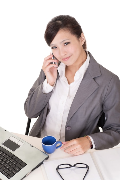 Femme d'affaires confiante à l'aide de téléphone portable et assis sur une chaise au bureau sur fond blanc.