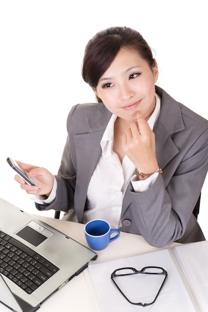 Femme d'affaires confiante à l'aide de téléphone portable et assis sur une chaise au bureau sur fond blanc.