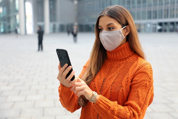 Femme d'affaires confiante portant un masque de protection appelant avec téléphone en se tenant debout près d'un immeuble de bureaux moderne à l'extérieur