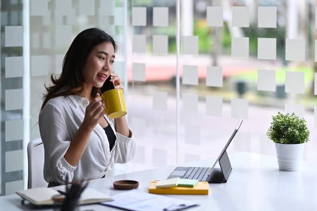 Femme d'affaires confiante tenant une tasse de café et parlant au téléphone portable.