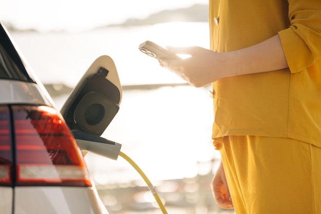 Femme d'affaires connecte la prise à la voiture électrique active l'application de charge sur le téléphone fille branche le câble d'alimentation