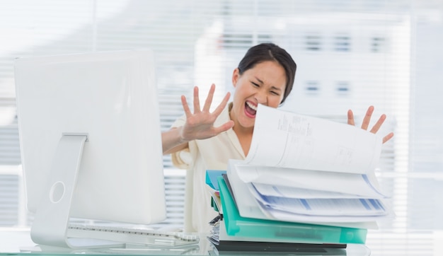 Femme d&#39;affaires criant avec une pile de dossiers au bureau