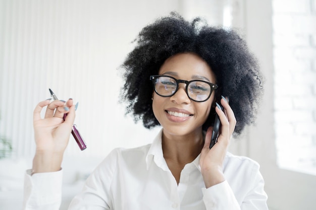 Une femme d'affaires dans un bureau avec des lunettes parle au téléphone en souriant et en montrant ses dents