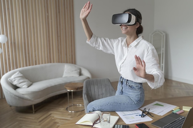 Femme d'affaires dans un casque VR sur la tête touchant des objets 3d tout en travaillant dans un bureau moderne