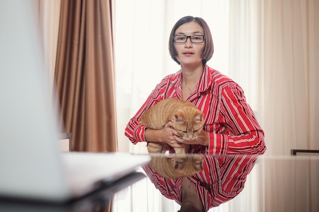 Femme d'affaires dans une chemise rouge avec un chat roux à la maison