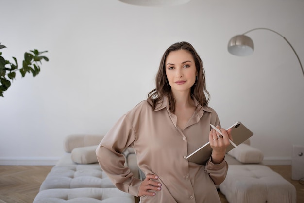 Une femme d'affaires dans un costume beige lâche tient une tablette numérique dans ses mains une photo à l'intérieur c