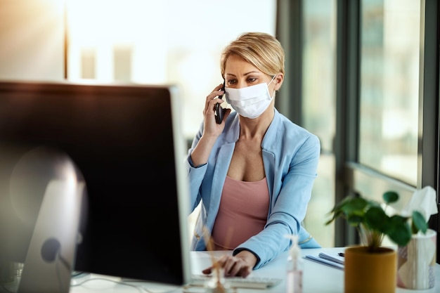 Femme d'affaires dans un masque de protection médicale travaille à l'ordinateur et parle sur un smartphone pendant l'auto-isolement et la quarantaine pour éviter l'infection pendant l'épidémie de virus de la grippe et l'épidémie de coronavirus