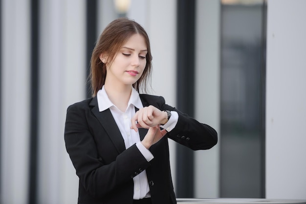 Une femme d'affaires dans la rue dans un costume formel regarde sa montre-bracelet vérifie l'heure sur sa montre