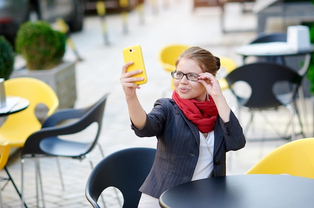 Femme d'affaires dans des verres assis à une table dans un café et fait Selfie