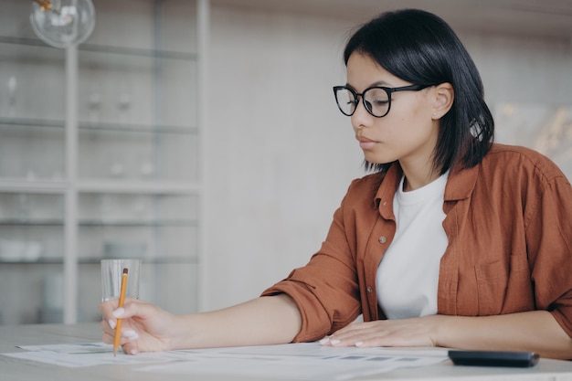 Une femme d'affaires dans des verres calcule les taxes sur les dépenses mensuelles assis au bureau du lieu de travail au bureau