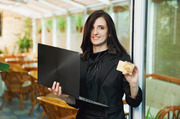 Femme d'affaires debout au restaurant avec ordinateur portable et montrant la carte de crédit