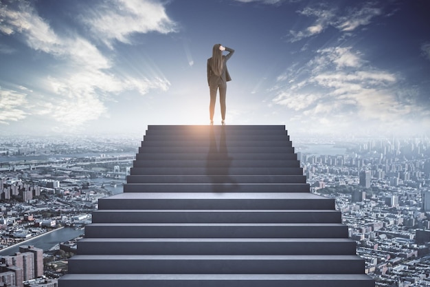 Femme d'affaires debout au sommet de l'escalier en béton pensant au-dessus de la ville Futur succès et concept de croissance