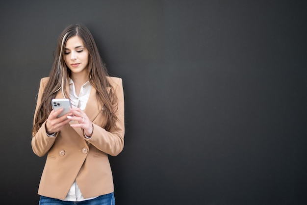 Femme d'affaires debout contre un tableau noir avec un smartphone à la main