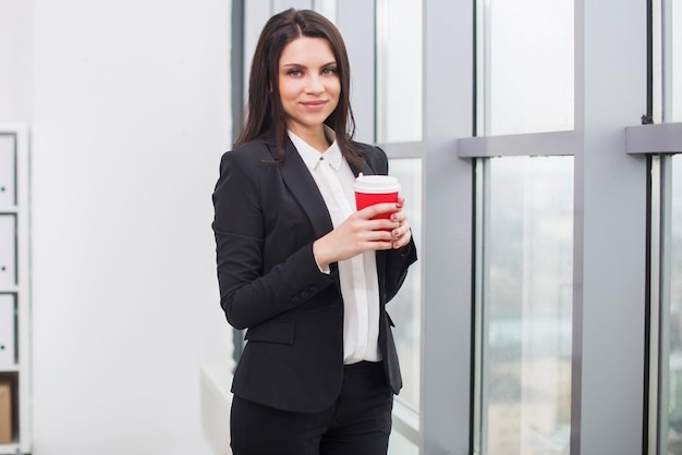 Femme d'affaires debout à la fenêtre avec une tasse