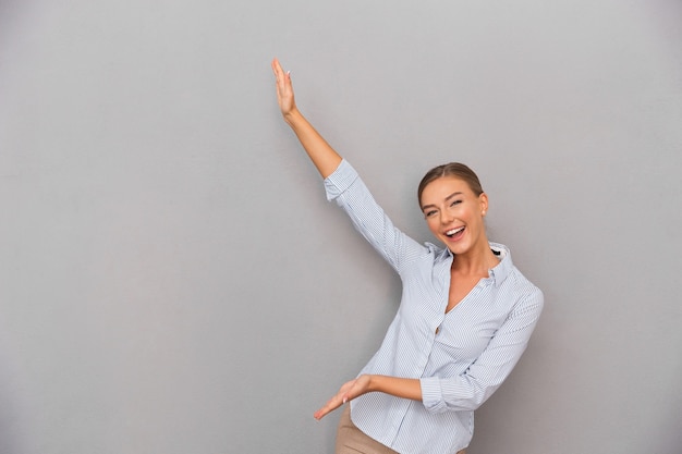 Femme d'affaires debout sur fond de mur gris posant montrant copyspace.