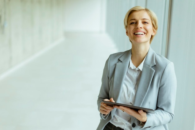 Femme d'affaires debout avec une tablette numérique dans le couloir du bureau