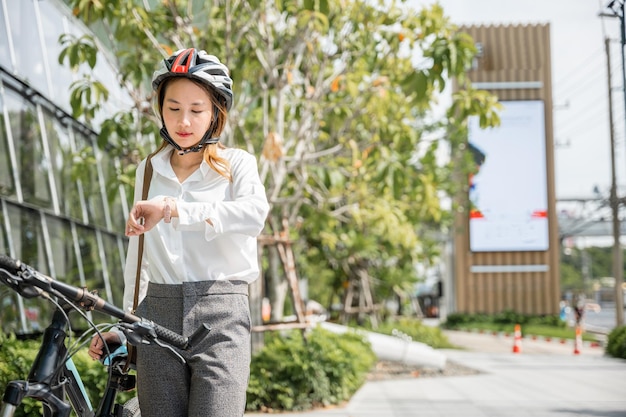 Femme d'affaires debout avec vélo vérifiant l'heure dans la rue de la ville