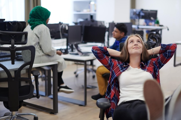 femme d'affaires décontractée prenant une pause avec les jambes sur sa table tout en travaillant sur un ordinateur de bureau dans un intérieur de bureau de démarrage à plan ouvert moderne