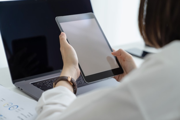 Femme d'affaires détenant l'écran de la tablette numérique vierge avec ordinateur portable et rapporte des graphiques financiers.