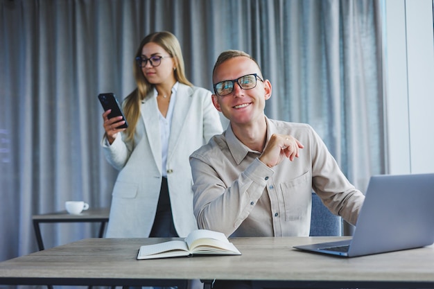 Une femme d'affaires devant un collègue masculin qui travaille sur un ordinateur portable Coopération commerciale et travail d'équipe Employés de bureau européens à la table du bureau Des gens modernes qui réussissent