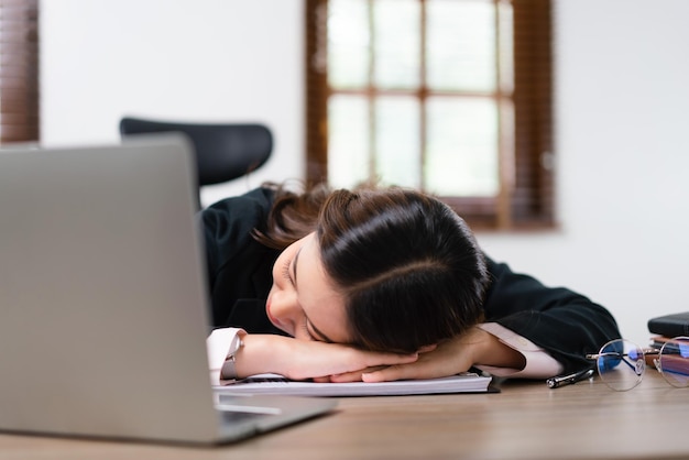 Femme d'affaires dormant sur son bureau près d'un ordinateur portable après avoir été épuisée par le surmenage au travail