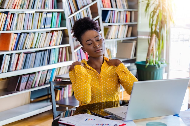 Femme d'affaires avec une douleur au cou assis à la table avec ordinateur portable