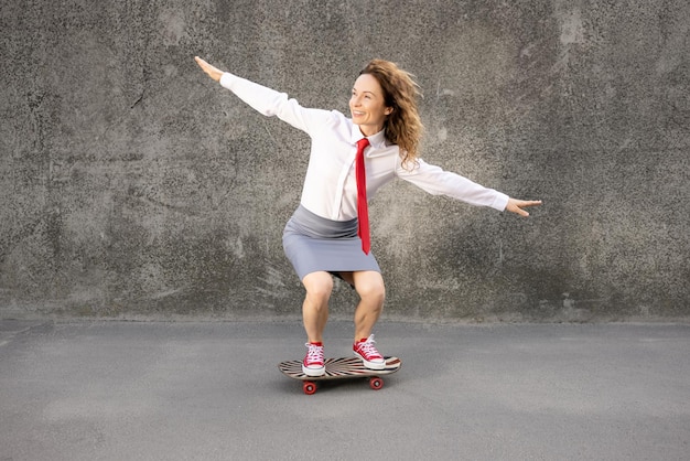 Femme d'affaires drôle faisant du skateboard en plein air