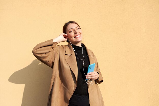 Photo femme d'affaires écoutant de la musique au téléphone contre le mur jaune