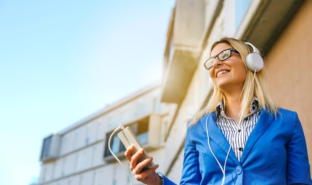 Photo une femme d'affaires écoute de la musique sur des écouteurs contre un immeuble de bureaux.