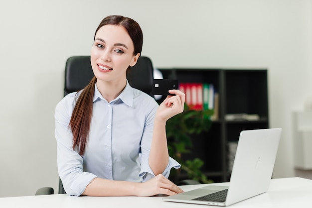 Femme d'affaires effectuant des paiements en ligne et virant de l'argent en utilisant une carte de crédit et un ordinateur portable au bureau