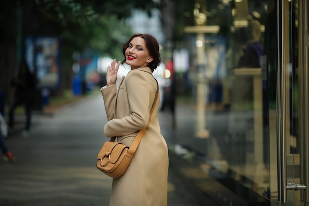 Femme d'affaires élégant de 25 ans dans un manteau blanc sur fond d'une rue avec des magasins