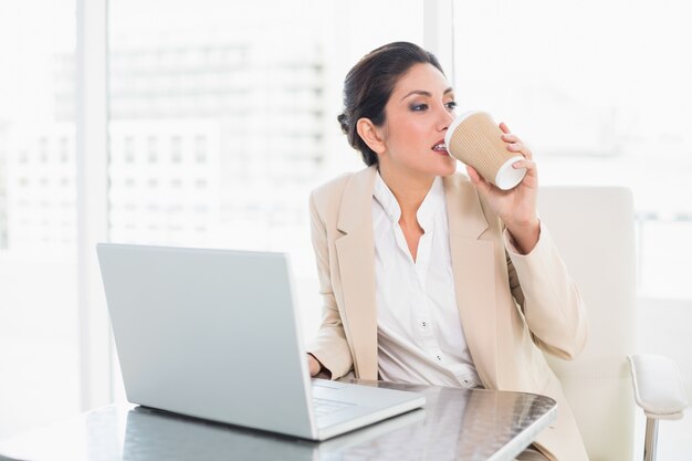 Femme d&#39;affaires élégant, boire du café tout en travaillant sur un ordinateur portable