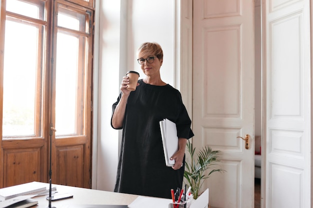 Une femme d'affaires élégante en robe noire tient une tasse de café