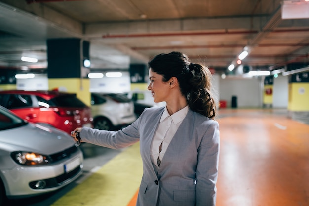 Femme d'affaires élégante verrouillant sa voiture avec des clés dans un parking souterrain.