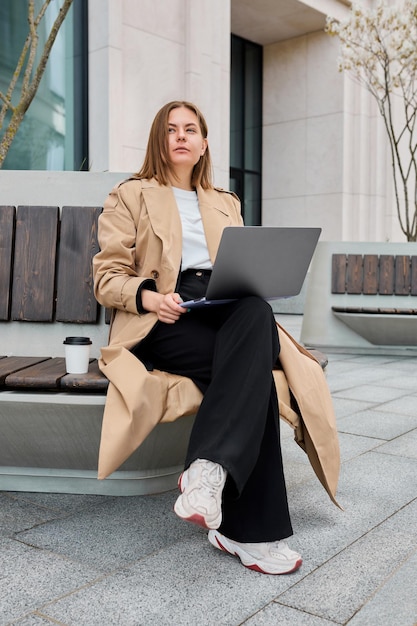 Une femme d'affaires embrasse la polyvalence de l'environnement de travail moderne en travaillant sans effort sur son ordinateur portable tout en étant assise sur un banc