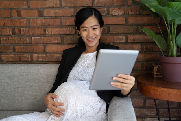 Femme d'affaires enceintes travaille assis sur un canapé à l'aide de tablette numérique