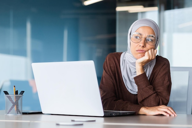 Femme d'affaires ennuyée sérieuse à l'intérieur du bureau femme musulmane en hijab pensant assise sur le lieu de travail