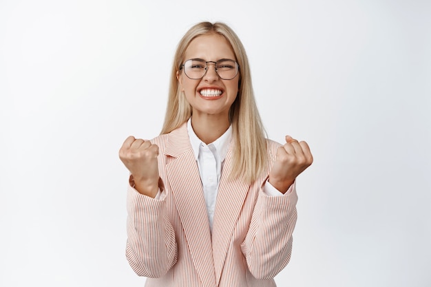 Une femme d'affaires enthousiaste serre les poings, l'air motivée et excitée, remportant une affaire, se tenant heureuse sur le blanc.