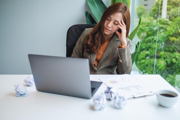 Une femme d'affaires est stressée par des papiers foutus et un ordinateur portable sur une table tout en ayant un problème au travail au bureau