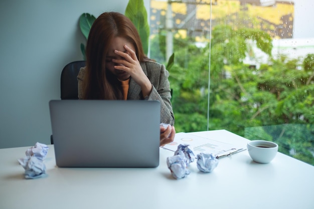 Une femme d'affaires est stressée par des papiers foutus et un ordinateur portable sur une table tout en ayant un problème au travail au bureau