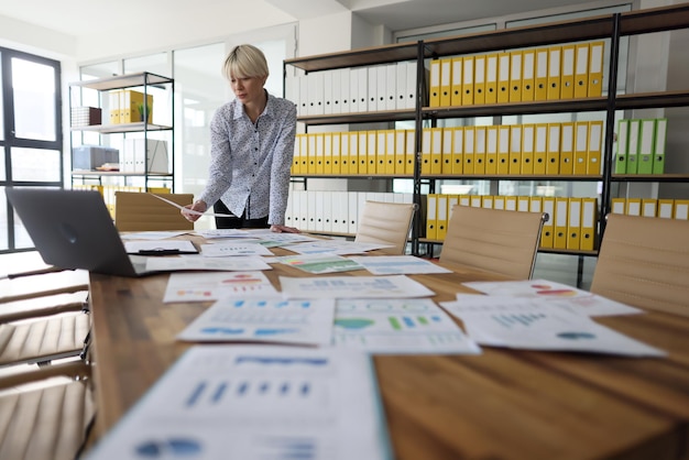 Une femme d'affaires examine des documents éparpillés se préparant à la présentation dans le patron du bureau de l'entreprise vide