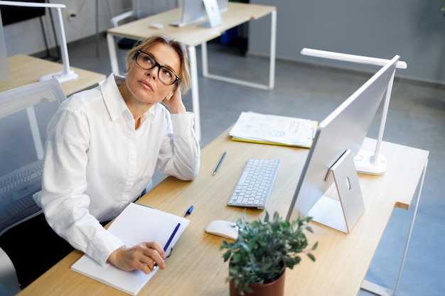 Femme d'affaires fatiguée en chemise blanche et lunettes assise à son bureau au bureau