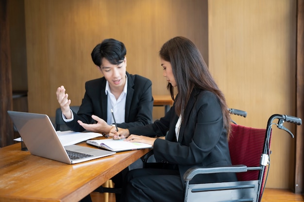 Femme d'affaires en fauteuil roulant travaillant sur un nouveau projet d'entreprise avec son collègue au bureau.