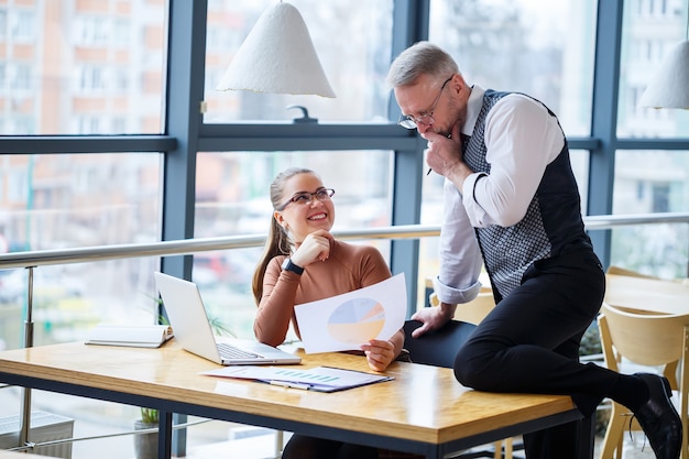 Femme d'affaires fille assise à une table en bois avec un ordinateur portable et discutant d'un nouveau projet avec son enseignant patron mentor. L'homme s'amuse. Nouveau concept de développement commercial