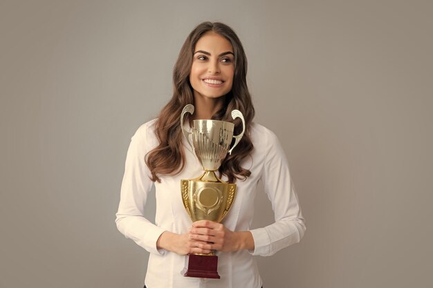 Femme d'affaires gagnante tenant un trophée Femme d'affaires avec prix Femme d'affaires avec coupe dorée et poing vers le haut gesticulant isolé sur gris