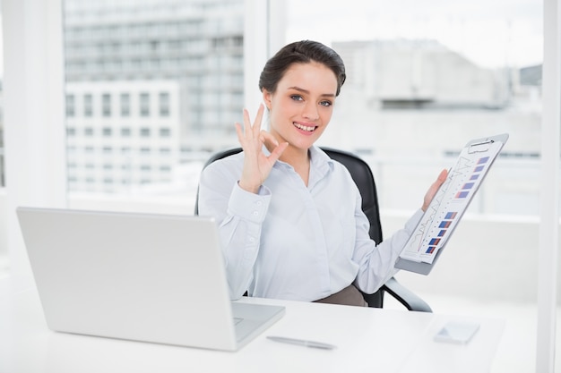 Femme d&#39;affaires avec des graphiques et ordinateur portable gesticulant signe correct au bureau