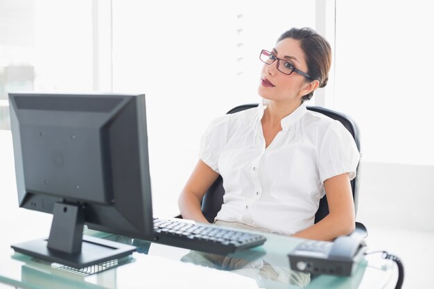 Femme d&#39;affaires grave assis à son bureau en regardant l&#39;ordinateur