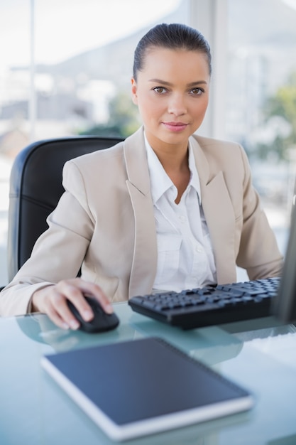 Femme d&#39;affaires grave travaillant sur ordinateur en regardant la caméra