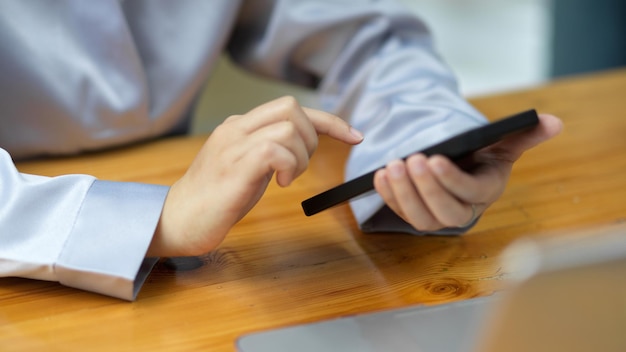 Femme d'affaires en gros plan utilisant un téléphone intelligent moderne sur son bureau pour jouer à des jeux mobiles, faire des achats en ligne et se détendre.