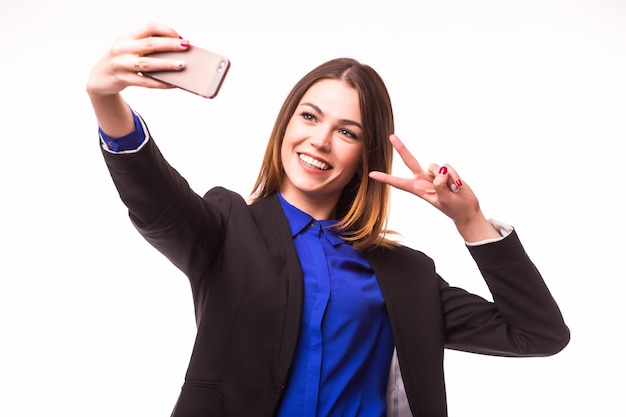 Femme d'affaires heureuse prenant smartphone photo selfie isolé sur mur blanc